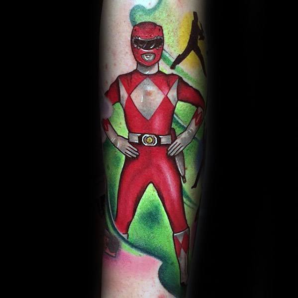 Full-body Red Ranger tattoo in classic pose with hands on hips, vibrant red suit, and green energy aura background on the forearm.