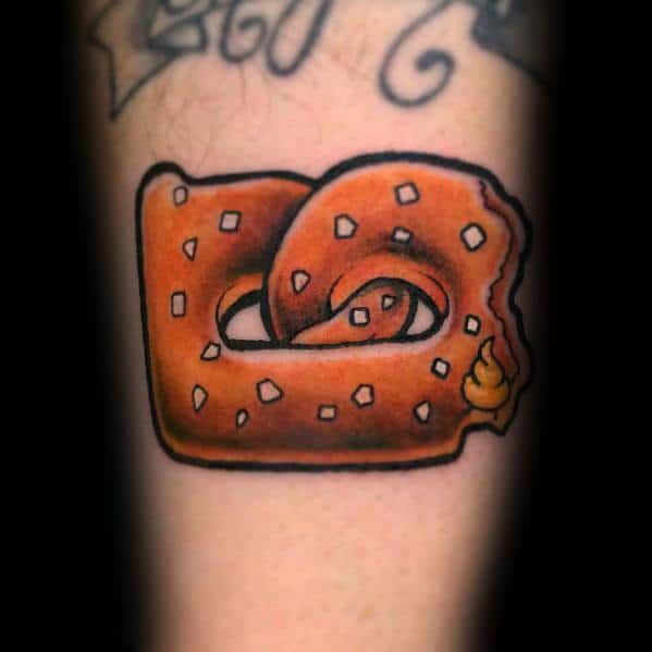 Square-shaped pretzel tattoo with salt details, a bite taken out, and mustard on the corner, featuring bold outlines and vibrant shading.