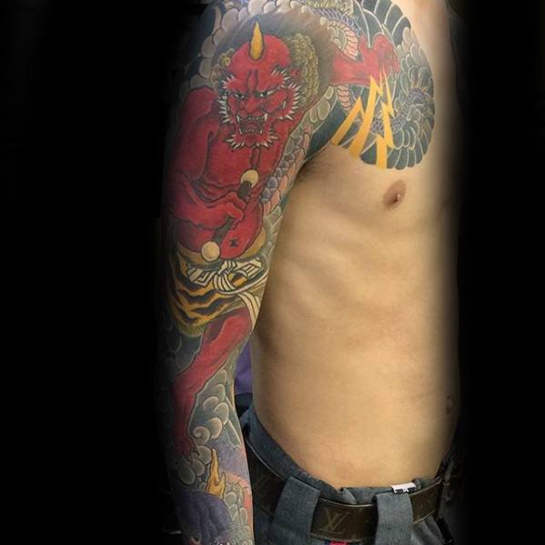 Dynamic Raijin full sleeve tattoo with fierce red thunder god, golden drumsticks, swirling clouds, and bold lightning detail.