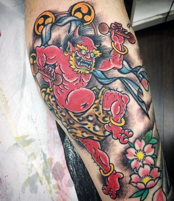 Playful Raijin tattoo with red thunder god, leopard-print shorts, golden rings, and floral accents in a bold Japanese cartoon style.