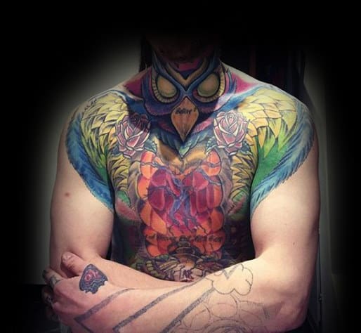 Throat and chest tattoo featuring a vibrant owl with piercing eyes, bold wings, and intricate colorful details blending into the body