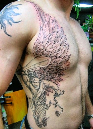 Man with an angel tattoo holding scales and sword on his chest and torso