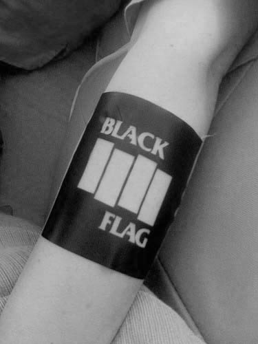 Bold blackout armband tattoo featuring negative space Black Flag bars with the words “BLACK” above and “FLAG” below in crisp block letters.