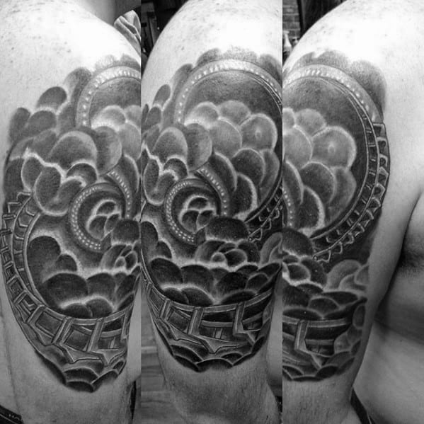 Black and grey roller coaster tattoo wrapping around the upper arm with dramatic clouds and deep shading for a 3D effect.