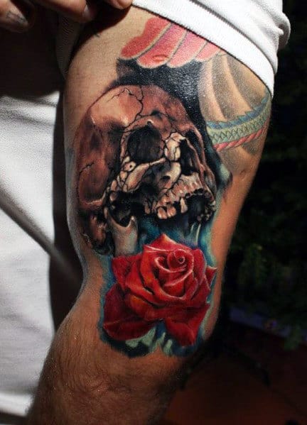 Realistic tattoo of a cracked skull with a vibrant red rose and blue accents, creating a striking contrast on the upper arm.
