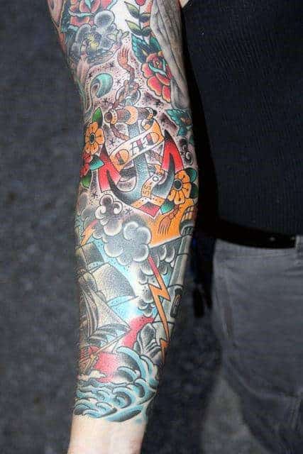 Colorful full sleeve tattoo with an anchor, flowers, ship, and lightning on arm