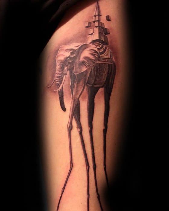 Realistic Salvador Dali-inspired tattoo of a surreal elephant with long, thin legs and a geometric obelisk structure on its back.