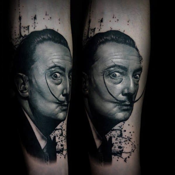 Realistic black and grey Salvador Dali tattoo with intense gaze, signature mustache, and abstract ink splatter detailing in the background.