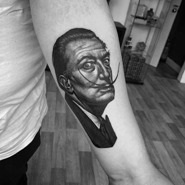 Black and grey Salvador Dali tattoo on the inner arm, featuring a sharp portrait with defined shadows and his iconic curled mustache.