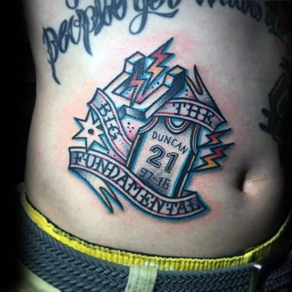 Colorful San Antonio Spurs tattoo on the ribs featuring Tim Duncan's jersey, lightning bolts, and a banner reading "THE BIG FUNDAMENTAL."