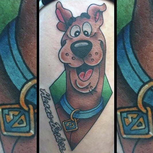 Tattoo of a smiling Scooby-Doo with his tag and collar, framed by a green diamond shape and cursive text reading “Hanna-Barbera.”
