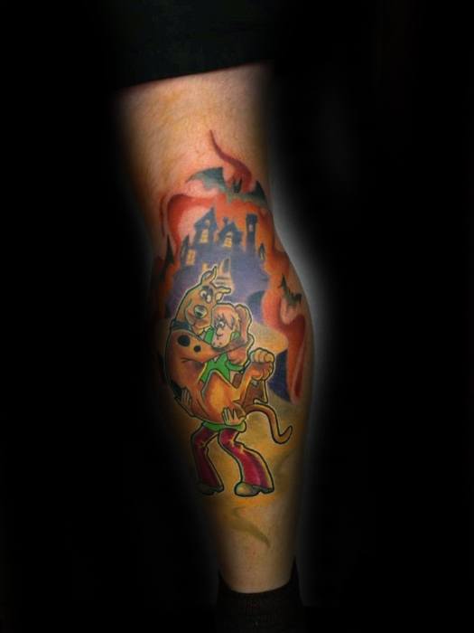 Tattoo of Shaggy hugging Scooby-Doo in fear with bats, fire, and a haunted castle in the background on the calf.