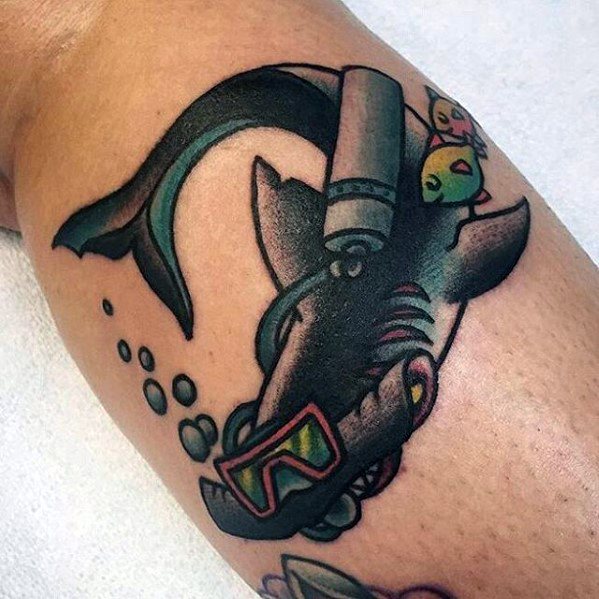 Playful cartoon-style tattoo of a shark wearing scuba gear with goggles and tank, accompanied by a small yellow fish on its back.