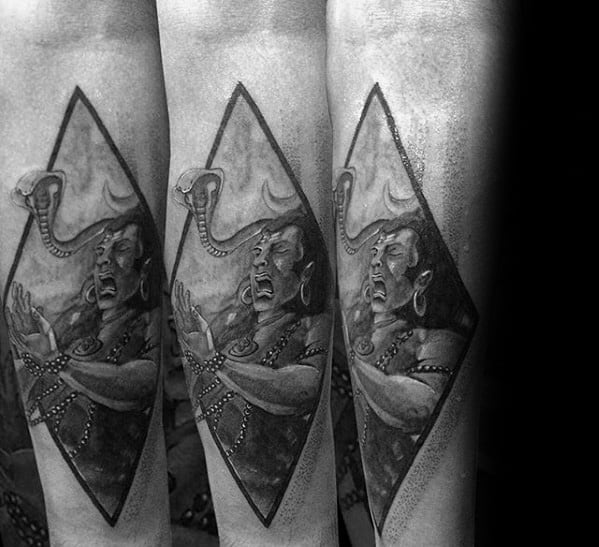 Forearm tattoo of fierce Lord Shiva inside a diamond frame, depicted in an intense pose with a raised arm and cobra emerging beside his head.