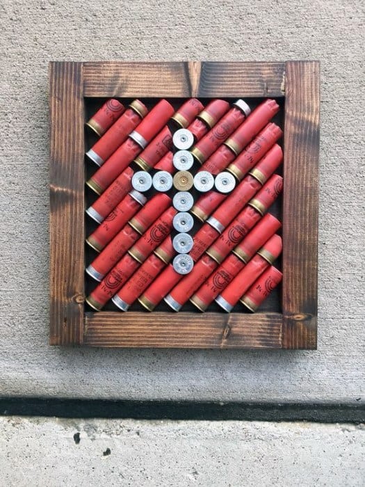 Rustic framed artwork featuring red shotgun shells arranged in a cross pattern for a bold statement.