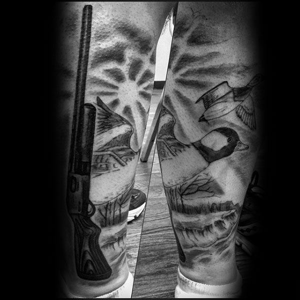 Black and grey hunting-themed tattoo featuring a shotgun, flying ducks, and a scenic outdoor background, detailed with fine shading and realism.