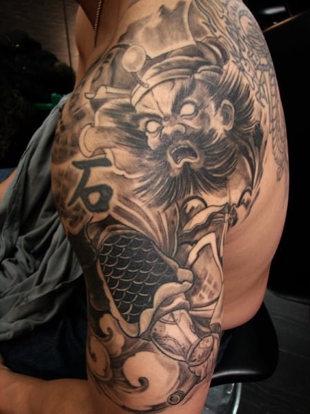 Detailed black and gray tattoo of a warrior with intricate designs on a person's arm