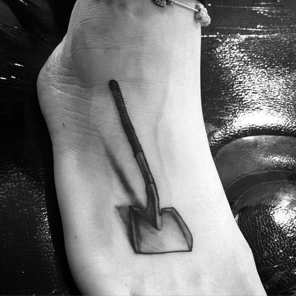 Black and grey shovel tattoo on the foot with a realistic design, featuring shading for depth, symbolizing hard work and perseverance.