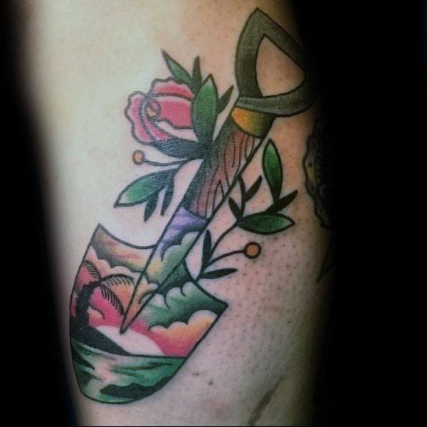 Colorful shovel tattoo featuring a tropical beach scene on the blade, with flowers and leaves around the handle, blending nature and adventure.