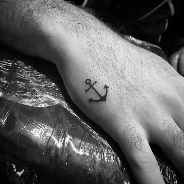 Small black anchor tattoo on the hand with a minimalist design, symbolizing strength, stability, and a deep connection to the sea.