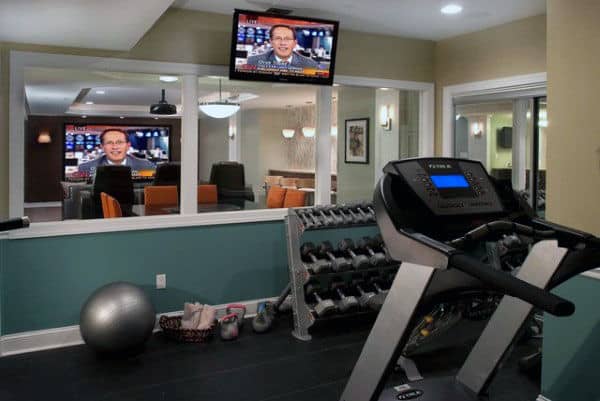 Home gym with treadmill, dumbbell rack, exercise ball, and TV in front of a mirror for ultimate home fitness