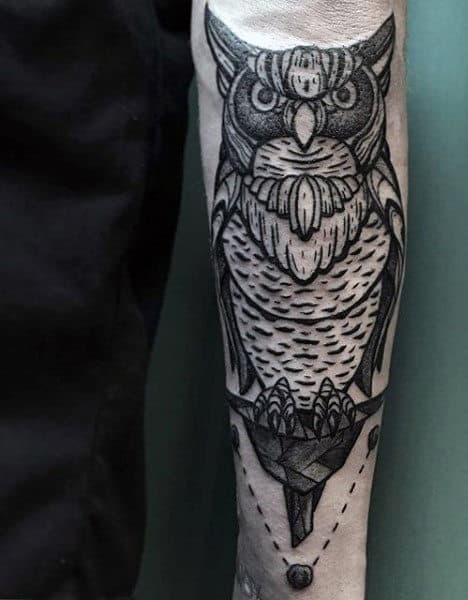 Forearm tattoo of a detailed, stylized owl with geometric accents and shading