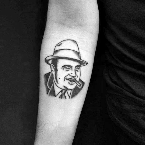 Al Capone tattoo featuring a simple black-and-white illustration of the gangster with a cigar, wearing his iconic fedora and suit.