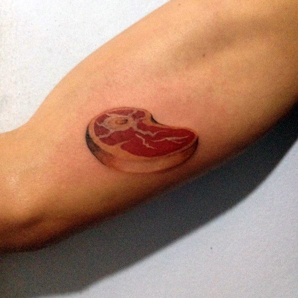 Tattoo of a small, realistic steak with rich marbling and shading, placed on the forearm for a minimalist yet bold meat-inspired design