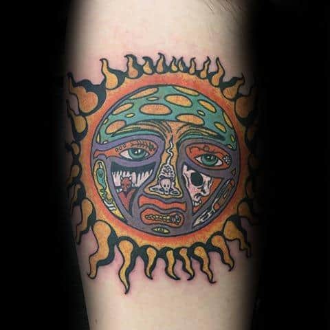 Colorful Sublime sun face tattoo with green, orange, and purple hues, framed by thick black flame rays and expressive features.