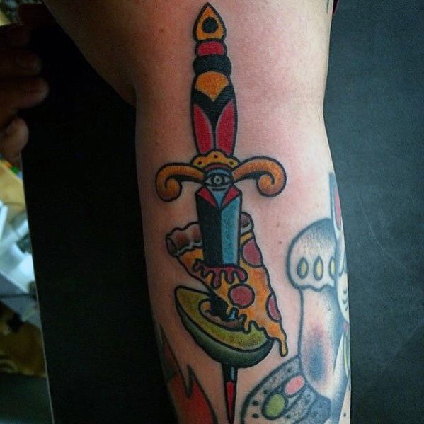 Traditional-style tattoo of a dagger piercing an avocado and pizza slice, combining bold lines, vibrant colors, and surreal humor.