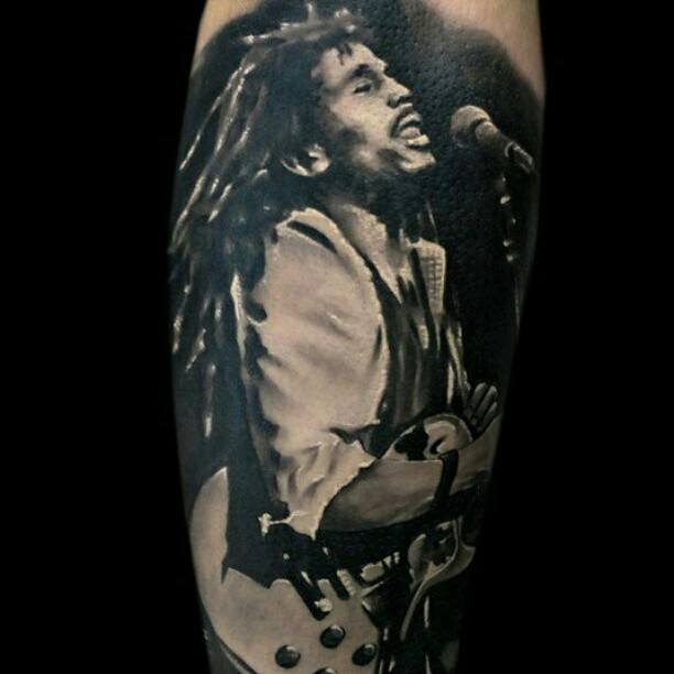 Black and gray tattoo of Bob Marley passionately singing and playing guitar on stage, capturing an iconic live performance moment.