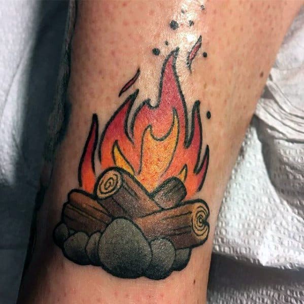 Bold campfire tattoo with bright orange and red flames, stacked logs, and a circle of shaded grey stones on the lower leg.