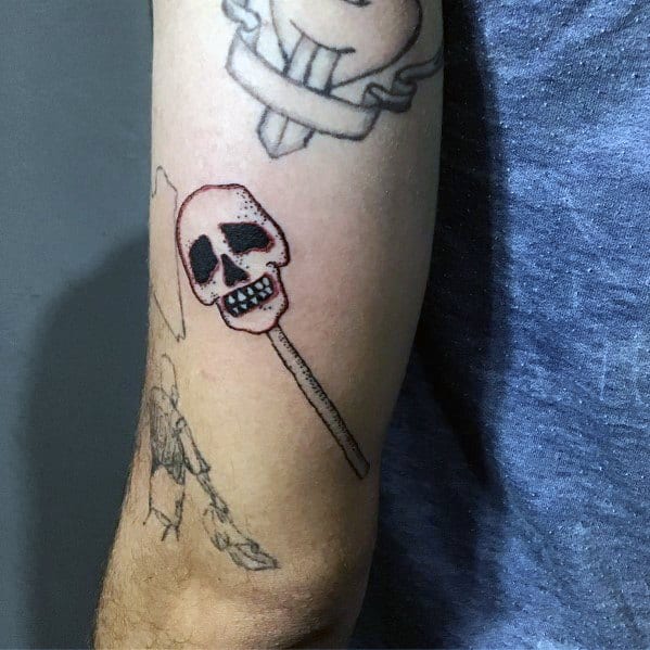 Minimalist skull lollipop tattoo with bold outlines and subtle shading, blending candy and macabre elements for a unique design on the arm.