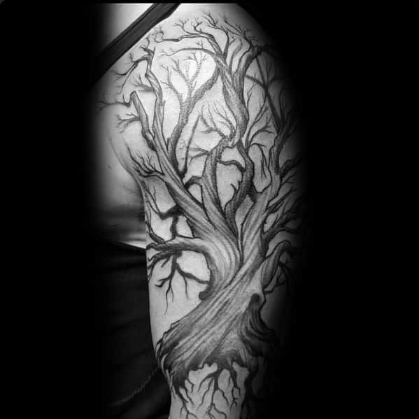 Black and grey upper arm tattoo of an ancient tree with twisted branches and deep roots, symbolizing strength, resilience, and growth.