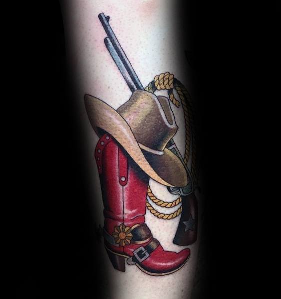 Tattoo of a cowboy hat resting on a red boot, with a rifle, rope, and spur, done in a bold Western style with vibrant colors and shading.