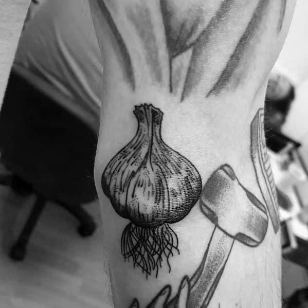 Black and grey garlic tattoo with fine shading and detailed roots, creating a bold and realistic botanical design on the arm.