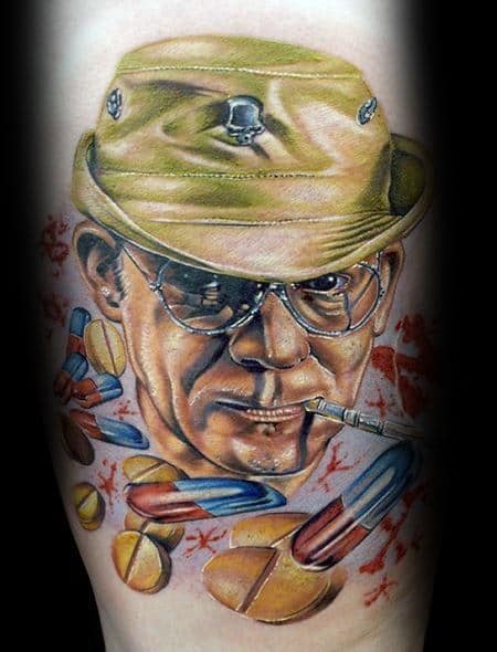 Realistic Hunter S. Thompson tattoo featuring a detailed portrait with aviator glasses, a military-style hat with a skull emblem, a cigarette, and scattered pills.