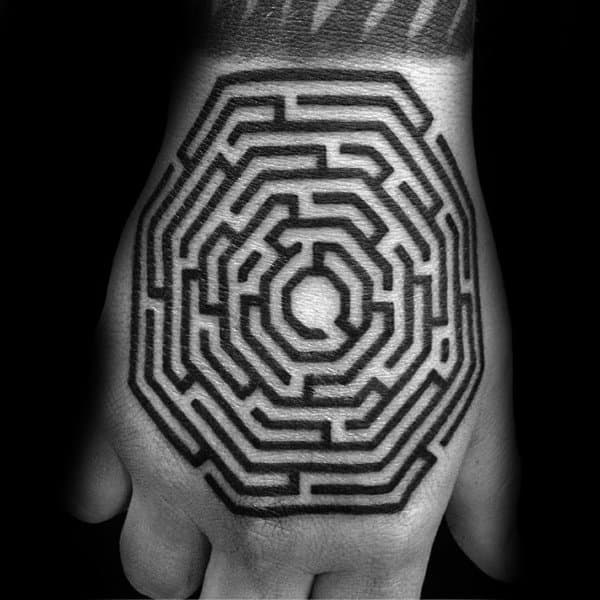 Bold black ink octagonal labyrinth tattoo on the back of a man's hand, featuring thick geometric lines forming a maze-like pattern.