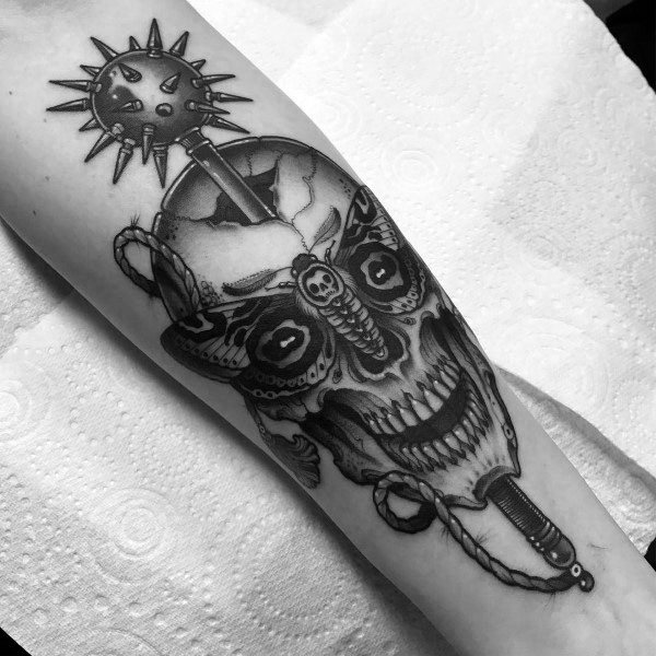 Black and gray tattoo featuring a detailed skull with a spiked mace embedded in it, symbolizing mortality, power, and the brutality of battle.
