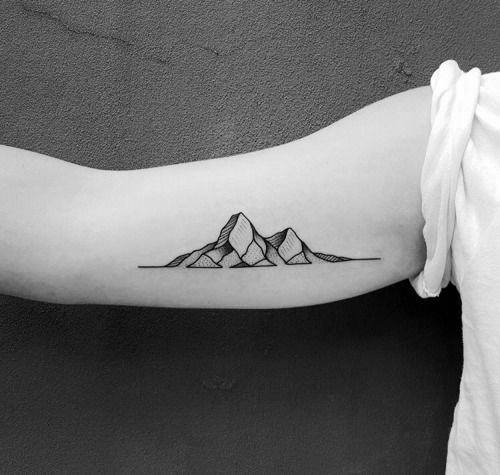 Minimalist mountain tattoo on the inner arm, featuring fine line peaks with geometric shading and a continuous horizontal line for a sleek design.