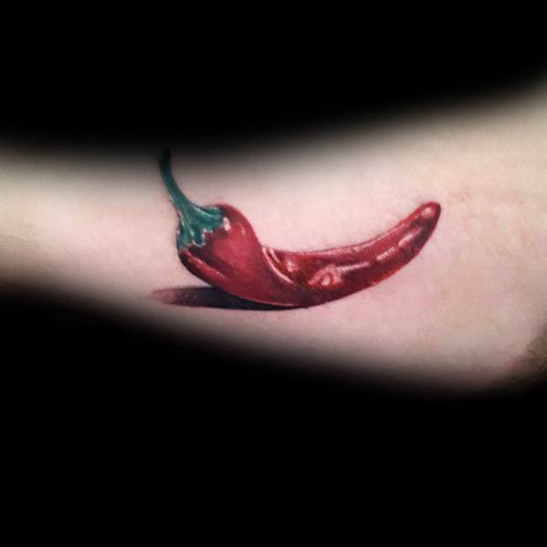 Realistic red chili pepper tattoo with a green stem and detailed shading, creating a glossy, three-dimensional effect on the skin.