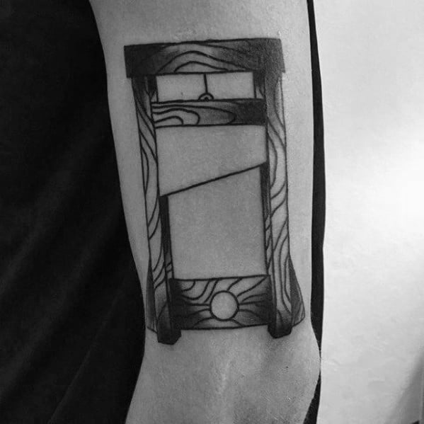 Minimalist guillotine tattoo with clean black lines, abstract wave-like wood patterns, and a bold, modern look on the inner arm.