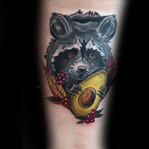 Traditional-style raccoon tattoo holding an avocado, with autumn leaves and berries, combining cute and bold elements in vibrant colors.