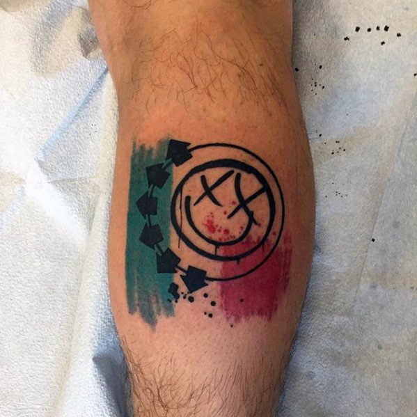 Tattoo of the Blink-182 smiley face logo with bold black lines, accompanied by teal and red watercolor splashes, placed on the lower leg.