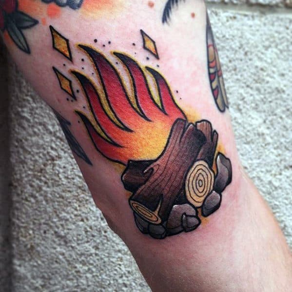 Traditional-style campfire tattoo with vivid flames, bold black outline, stacked logs, and glowing embers surrounded by stones.