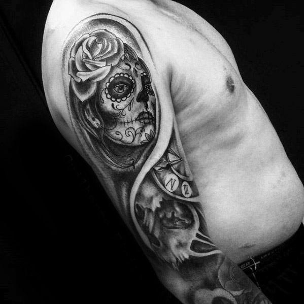 La Catrina upper arm tattoo of a woman with sugar skull makeup, a rose on her head, and a compass and dove below in black and grey.