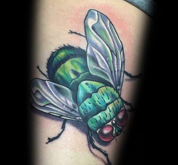 Hyper-realistic fly tattoo with vibrant green and teal tones, reflective wings, and bold red eyes for a striking 3D effect on skin.
