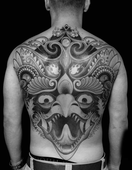 Full back Garuda tattoo in bold black and grey, featuring a fierce open-beaked face with symmetrical ornamental details and sharp contrast.