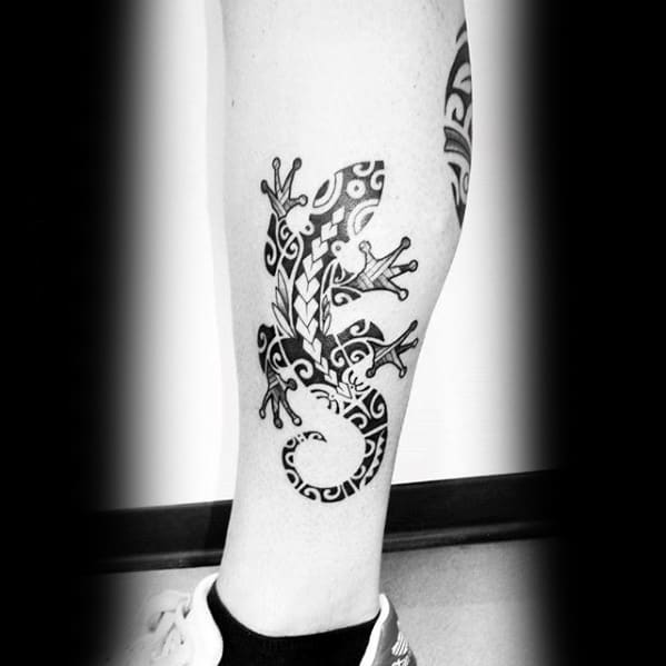 Black tribal gecko tattoo on calf with swirling patterns, leaf motifs, and a curled tail, combining bold and fine linework.