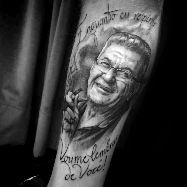 Tattoo of a smiling man with glasses and the words "Enquanto eu respirar, vou me lembrar de você!
